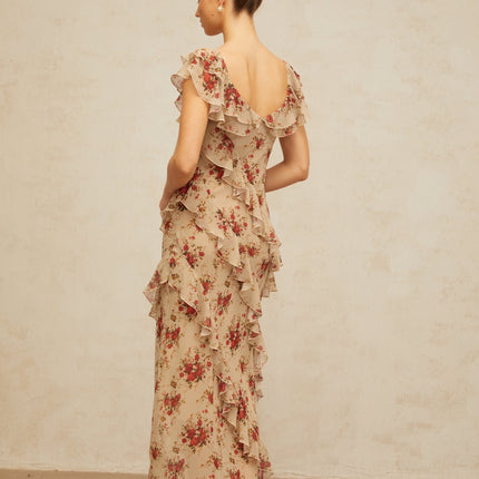 A woman wearing a long floral print maxi dress with ruffles and a flared skirt standing in a garden setting