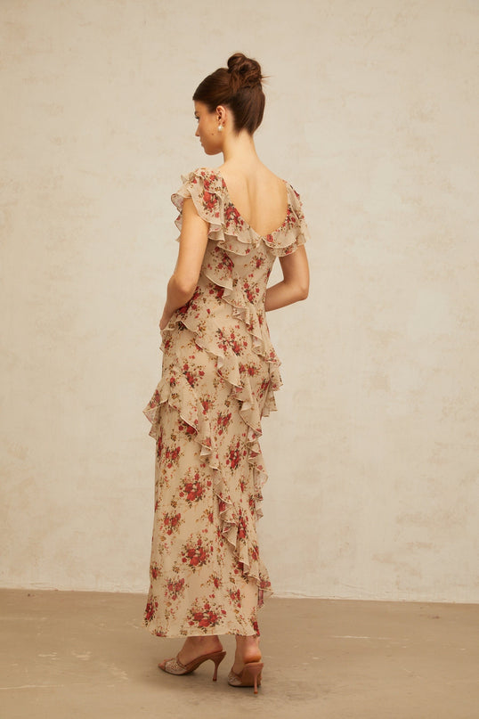 A woman wearing a long floral print maxi dress with ruffles and a flared skirt standing in a garden setting