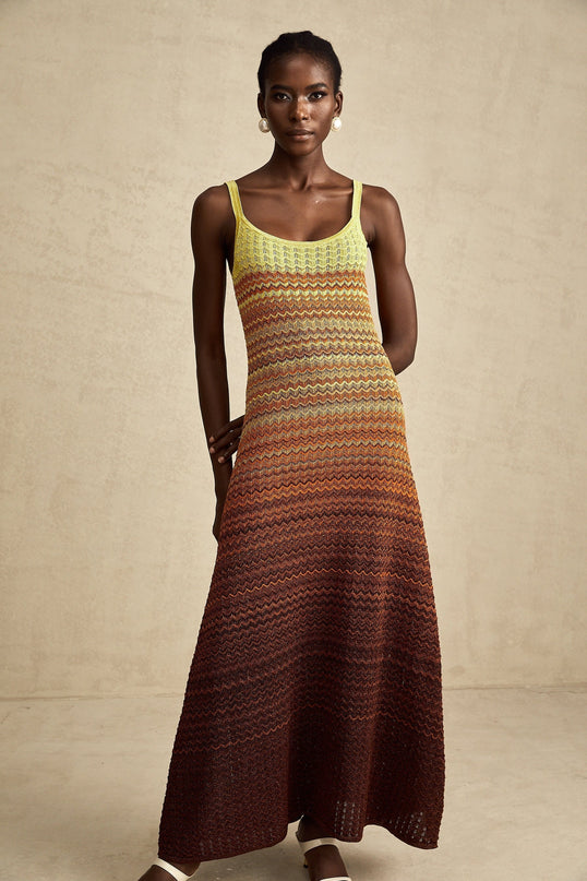 A woman wearing a long flowing knitted maxi dress with a gradient color pattern from light to dark shades standing in a relaxed pose