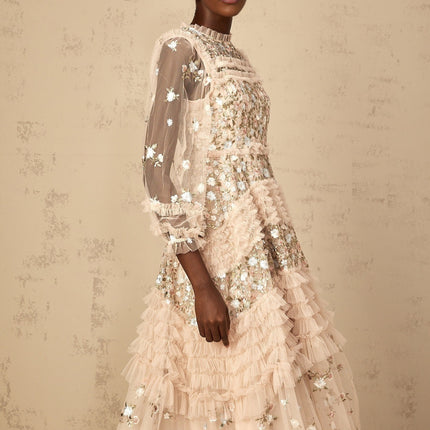 A woman wearing a long flowy maxi dress with tiered tulle skirt and floral embroidery details standing in an elegant pose