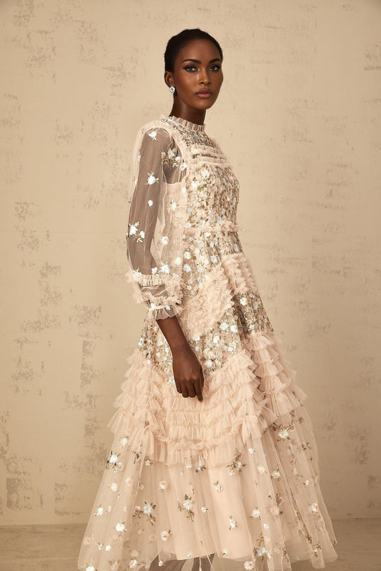 A woman wearing a long flowy maxi dress with tiered tulle skirt and floral embroidery details standing in an elegant pose