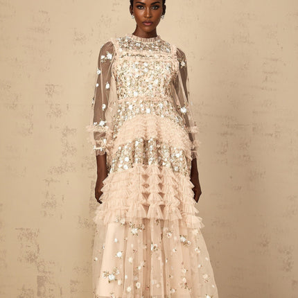 A woman wearing a long flowy maxi dress with tiered tulle skirt and floral embroidery details standing in an outdoor setting