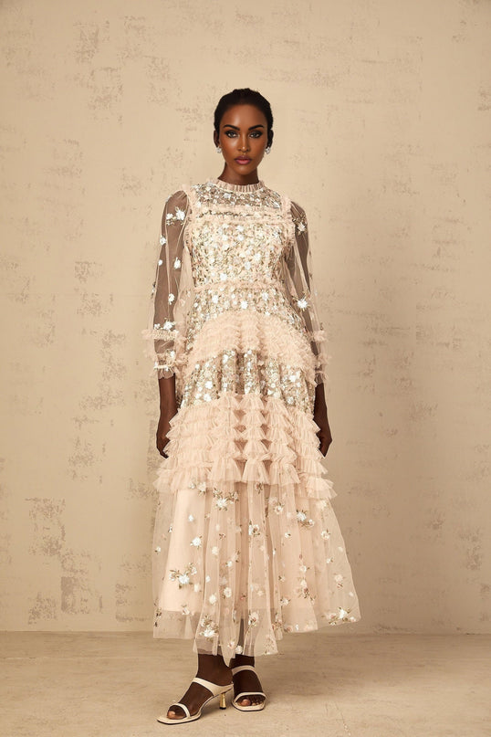 A woman wearing a long flowy maxi dress with tiered tulle skirt and floral embroidery details standing in an outdoor setting