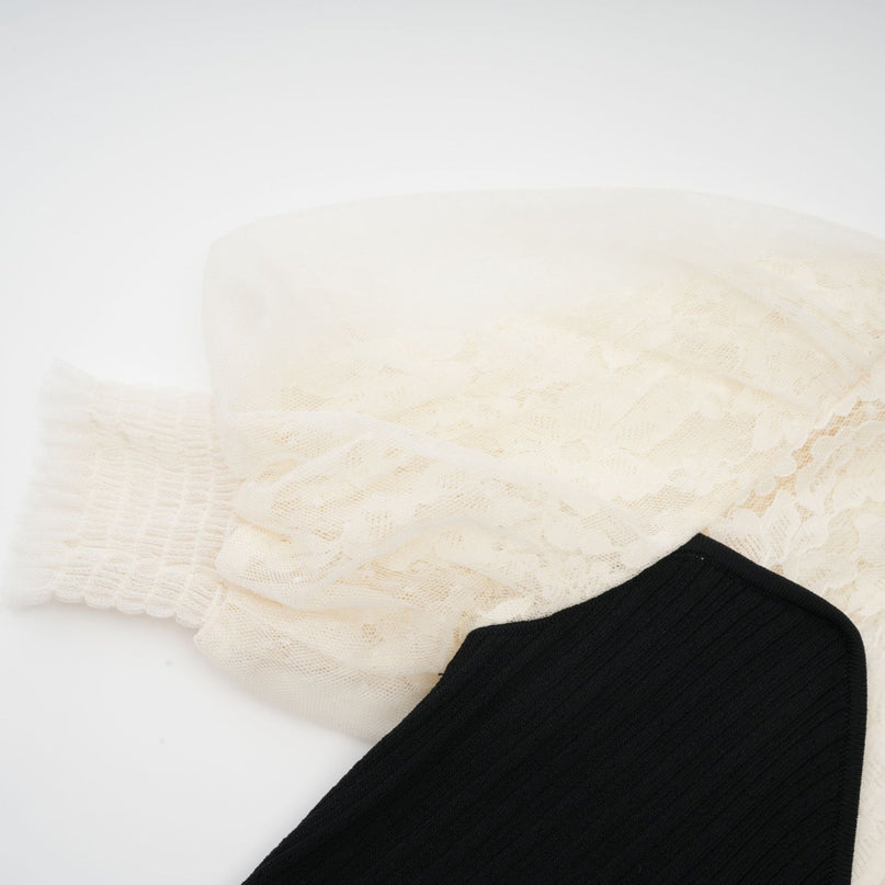 A woman wearing a long knit dress with lace trim detailing at the neckline and hem standing in a neutral pose against a plain background