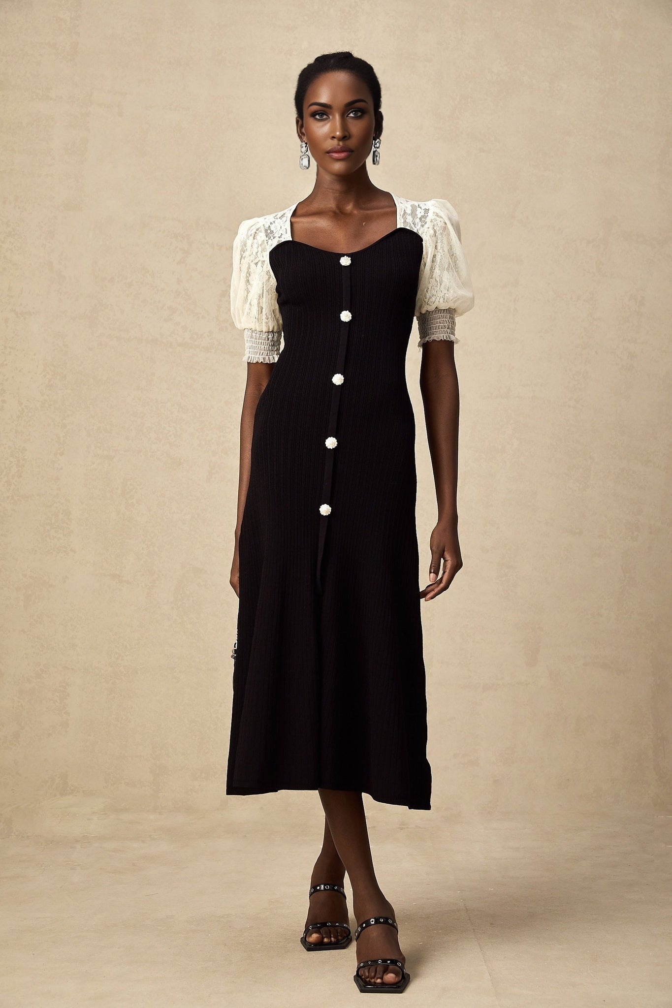 A woman wearing a long knit midi dress with lace trim details at the neckline and hem standing in a neutral pose