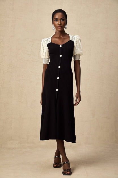 A woman wearing a long knit midi dress with lace trim details at the neckline and hem standing in a neutral pose