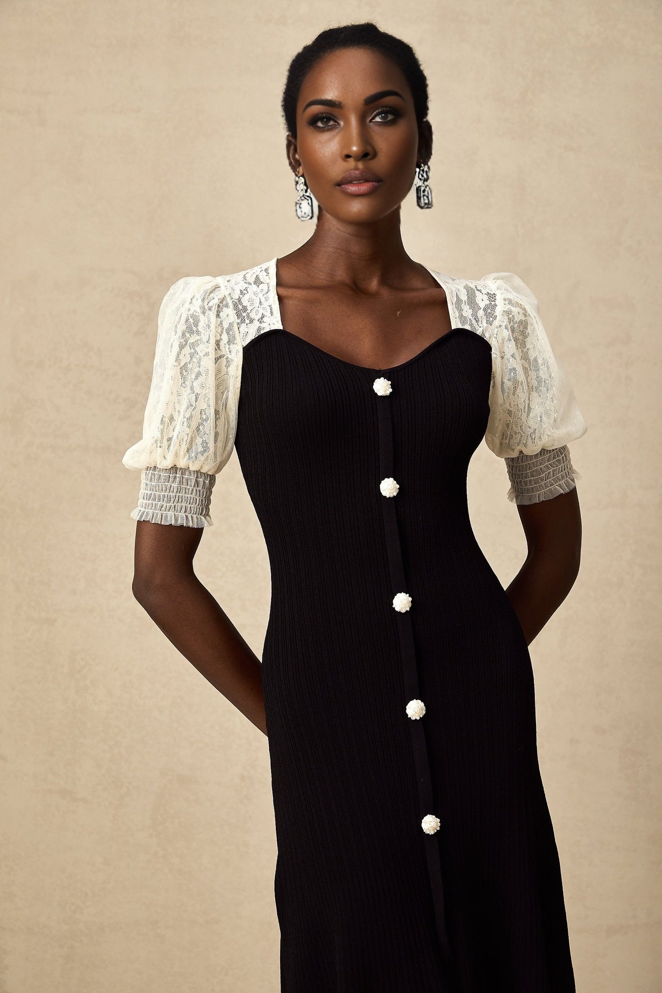 A woman wearing a long knit midi dress with lace trim details at the neckline and hem standing in a neutral pose
