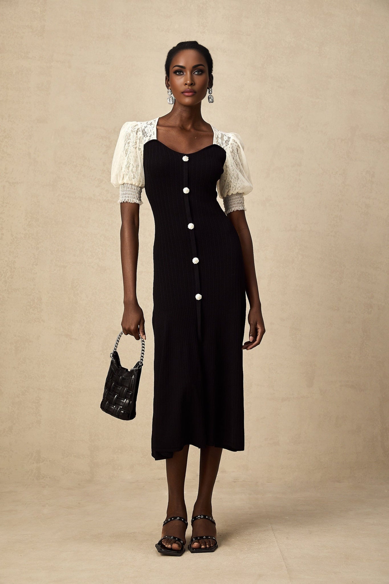 A woman wearing a long knit midi dress with lace trim details at the neckline and hem standing in a relaxed pose against a plain background
