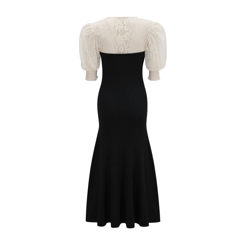 A woman wearing a long knit midi dress with lace trim details standing in a neutral setting