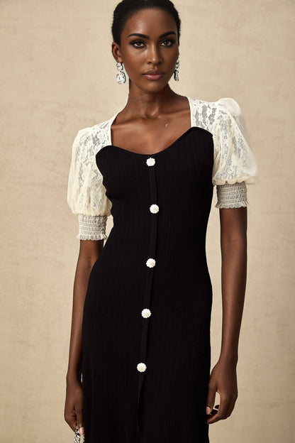 A woman wearing a long knitted midi dress with lace trim details at the neckline and hem standing in a relaxed pose against a plain background