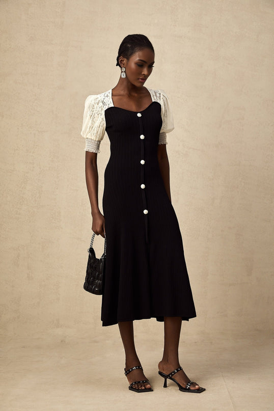 A woman wearing a long knitted midi dress with lace trim details standing in a relaxed pose