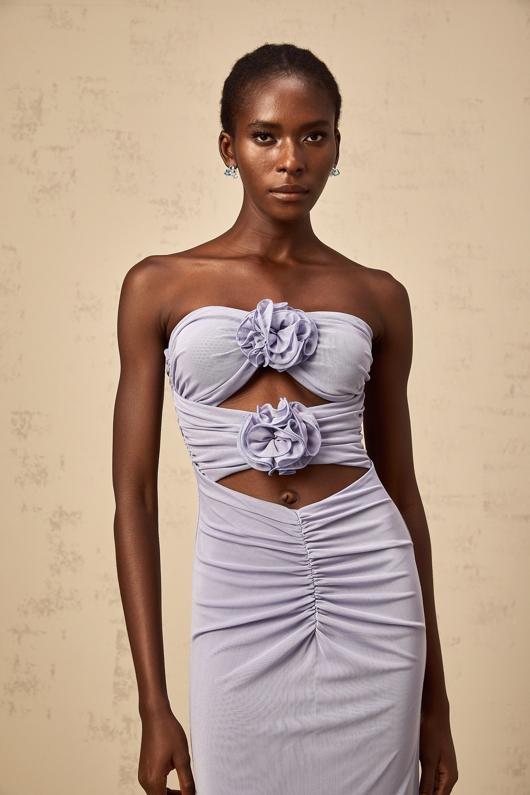 A woman wearing a long lavender dress with a fitted corset bodice and ruched 3D petal details flowing into a full maxi skirt