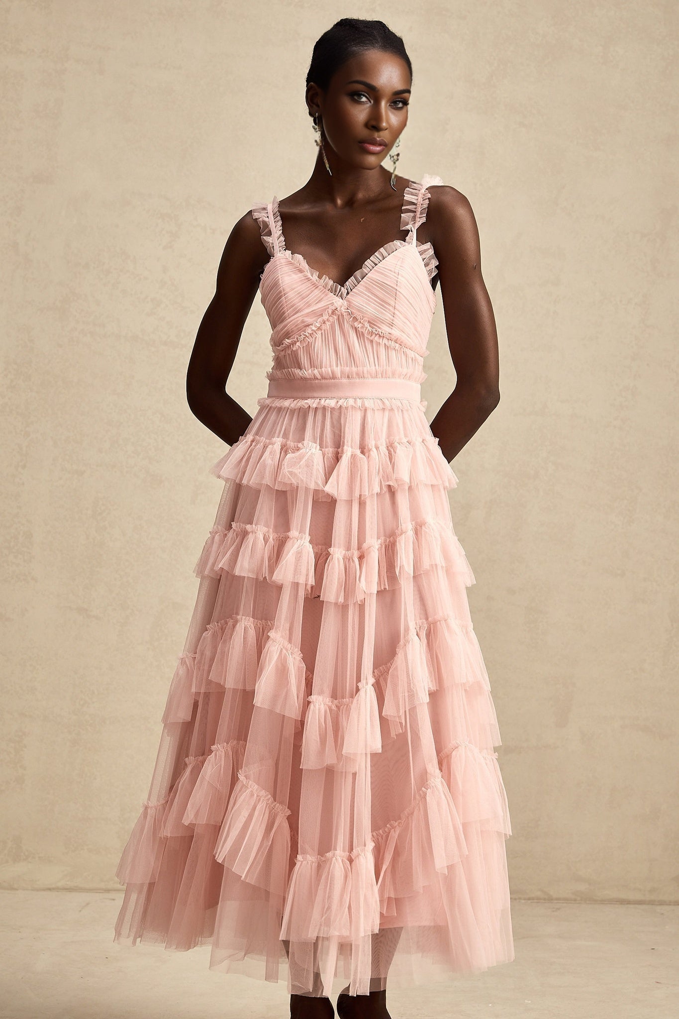 A woman wearing a long light colored maxi dress with multiple layers of ruffled tulle fabric creating a flowing and romantic silhouette