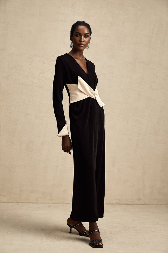 A woman wearing a long maxi dress with a vneck and a contrasting bow detail at the waist The dress features two different colors and has a flowing silhouette