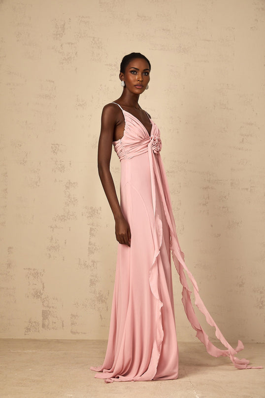 A woman wearing a long pink maxi dress with 3D floral petal details on the tulle fabric standing in an elegant pose
