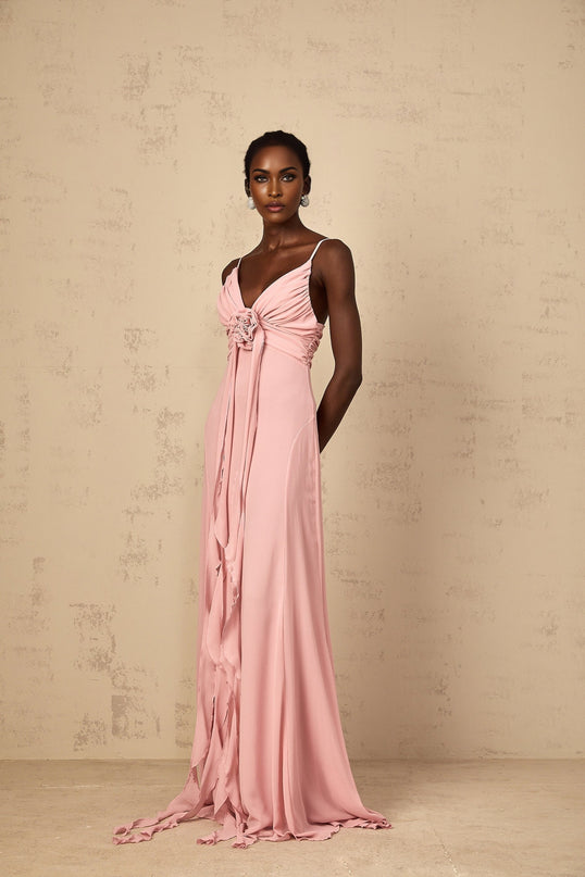 A woman wearing a long pink maxi dress with 3D floral petal details on the tulle skirt