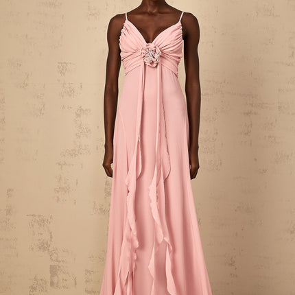 A woman wearing a long pink maxi dress with 3D petal details on the tulle fabric standing against a plain background