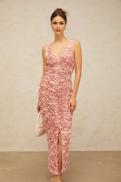 A woman wearing a long pink maxi dress with a Vneckline and floral pattern standing in a relaxed pose against a plain background