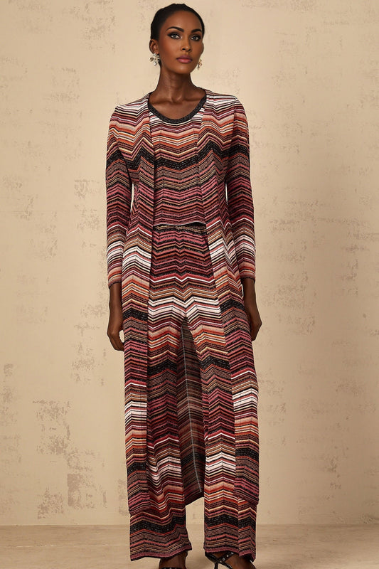 A woman wearing a long red cardigan with white stripes standing against a plain background The cardigan has a relaxed fit and reaches below the knees