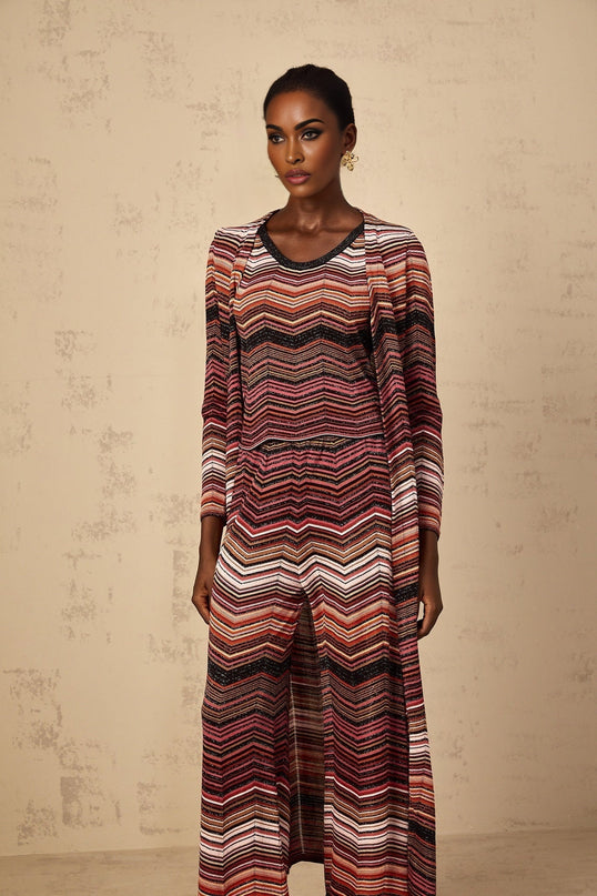 A woman wearing a long red cardigan with white stripes standing against a plain background