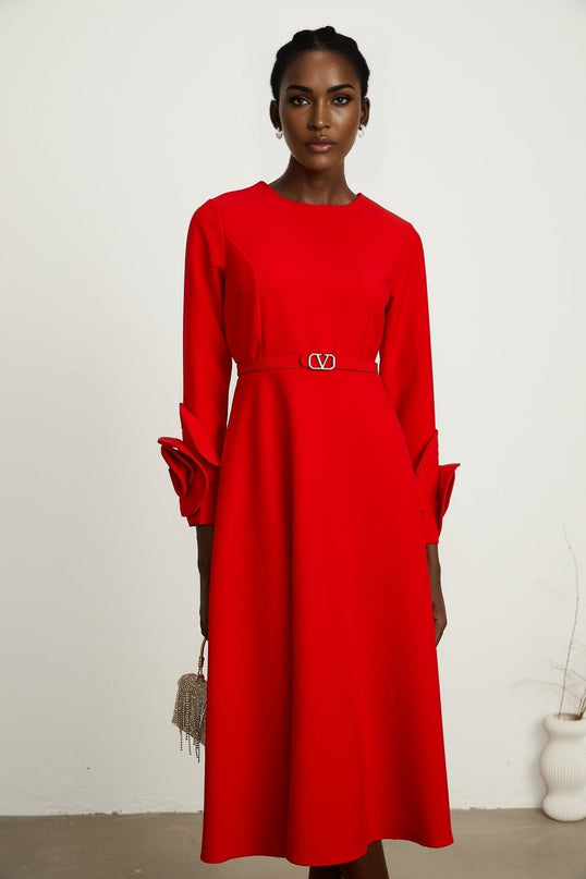 A woman wearing a long red dress with floral patterns and long sleeves