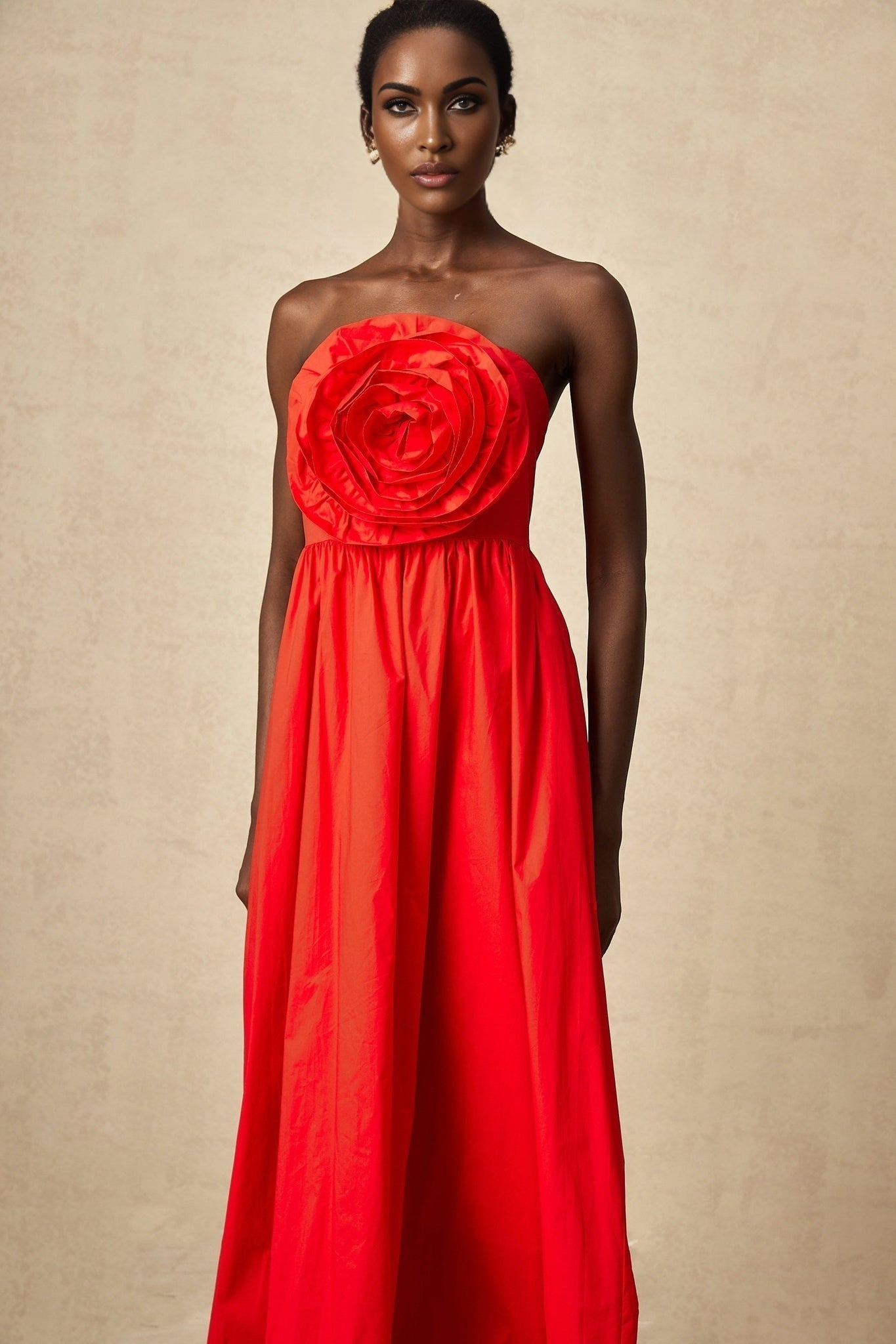 A woman wearing a long red dress with layered 3d petal ruffles cascading down the skirt creating a dramatic and flowing silhouette