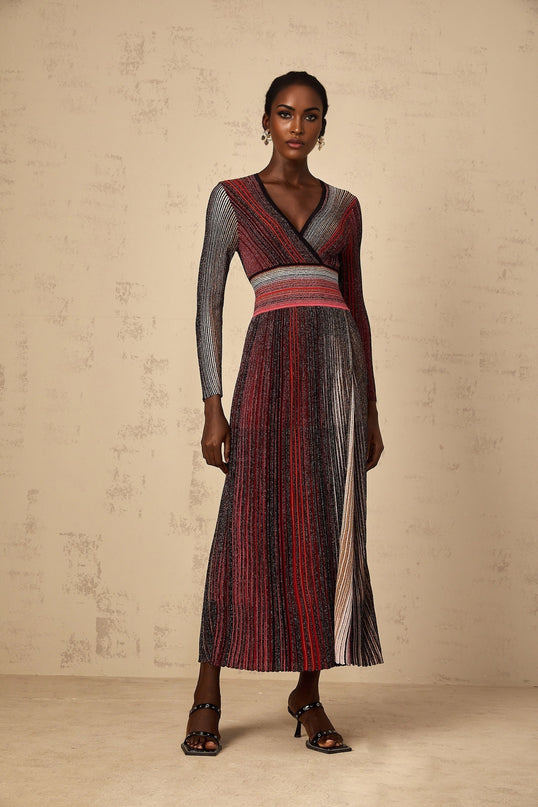 A woman wearing a long red maxi dress with long sleeves and vertical sequin stripes that shimmer in the light The dress has a knit texture and flows to the floor