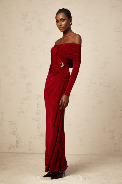 A woman wearing a long red velvet dress with ruched detailing and a fitted silhouette