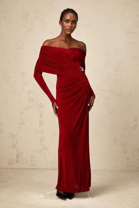 A woman wearing a long red velvet dress with ruched detailing and a fitted silhouette