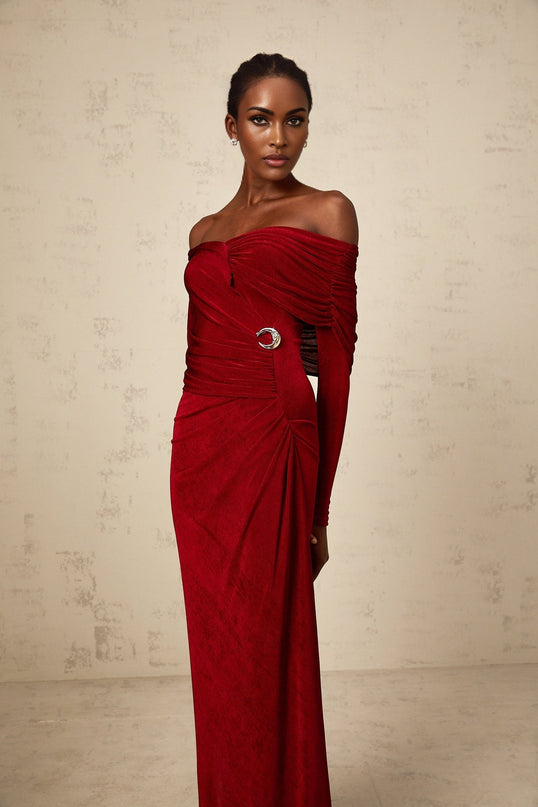 A woman wearing a long red velvet dress with ruched detailing and a fitted silhouette