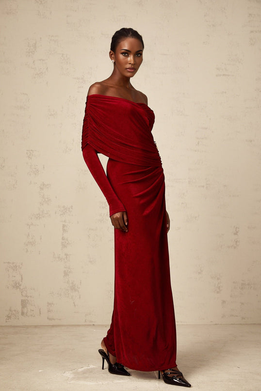 A woman wearing a long red velvet dress with ruched detailing and a fitted silhouette