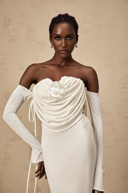 A woman wearing a long strapless maxi dress with a floral pattern The dress is ruched and features floral applique details It has a fitted bodice and flows out into a full skirt