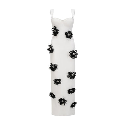 A woman wearing a long white bandage dress with floral applique detailing standing against a plain background
