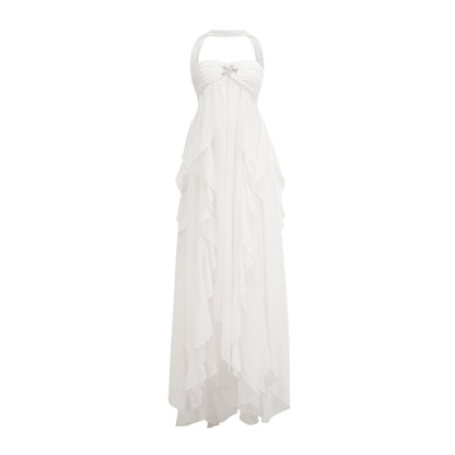 A woman wearing a long white chiffon maxi dress with ruffles and a halter neckline