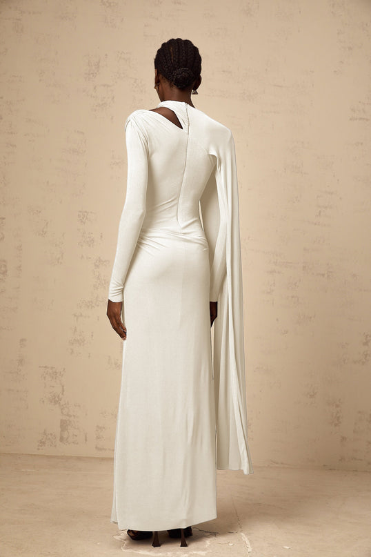 A woman wearing a long white fitted maxi dress with a diagonal shawl detail across the bodice