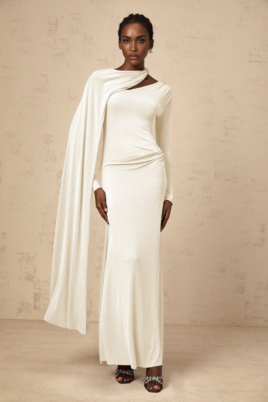 A woman wearing a long white fitted maxi dress with a diagonal shawl neckline