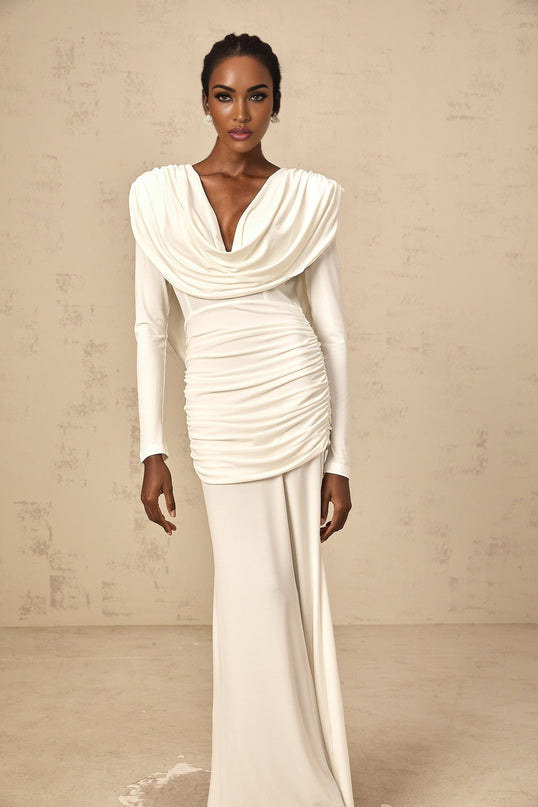 A woman wearing a long white fitted maxi dress with ruched detailing standing in a relaxed pose