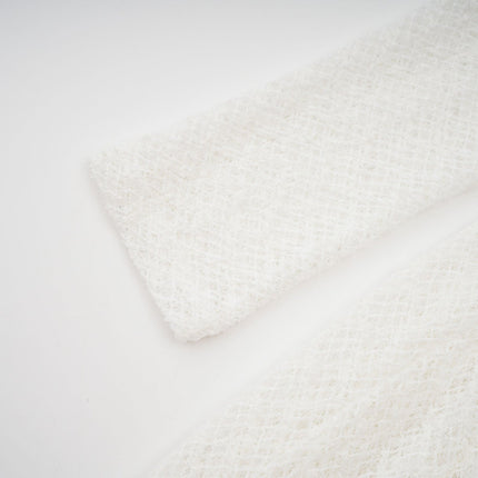 A woman wearing a long white lace maxi dress with a wavy pattern design standing against a plain background