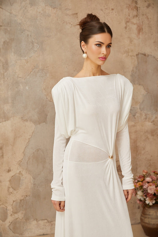 A woman wearing a long white maxi dress with draped and shirred details standing in a neutral setting