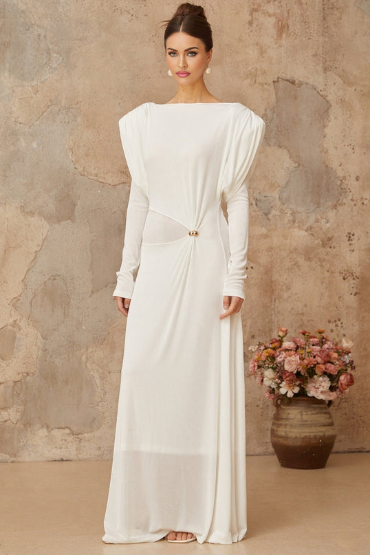 A woman wearing a long white maxi dress with draped and shirred details standing in a relaxed pose