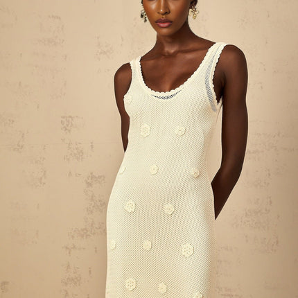 A woman wearing a long white maxi dress with floral embroidery and crochet knit details standing in a garden setting