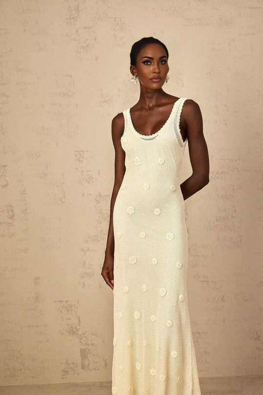 A woman wearing a long white maxi dress with floral embroidery and crochet knit details standing in an outdoor setting