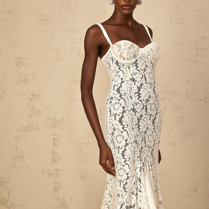 A woman wearing a long white maxi dress with floral lace detailing and a bustier style top