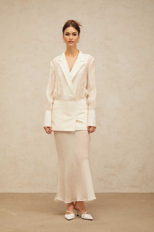 A woman wearing a long white maxi dress with semi sheer panelling standing against a plain background