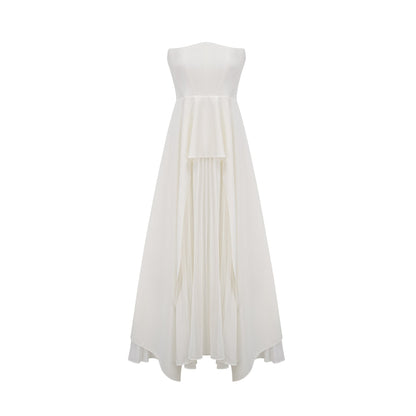 A woman wearing a long white pleated maxi dress with an offshoulder neckline