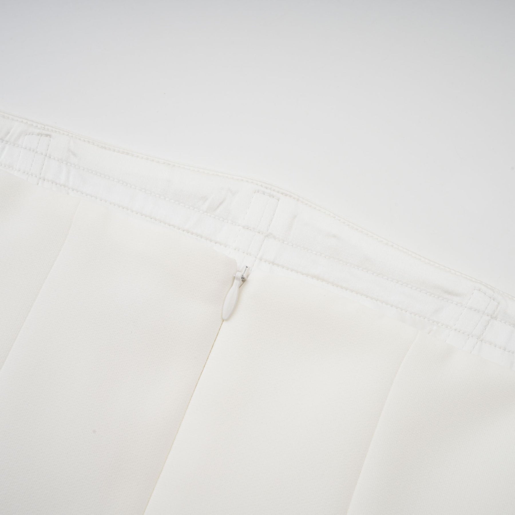 A woman wearing a long white pleated maxi dress with an offshoulder neckline