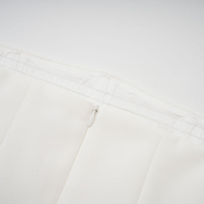 A woman wearing a long white pleated maxi dress with an offshoulder neckline