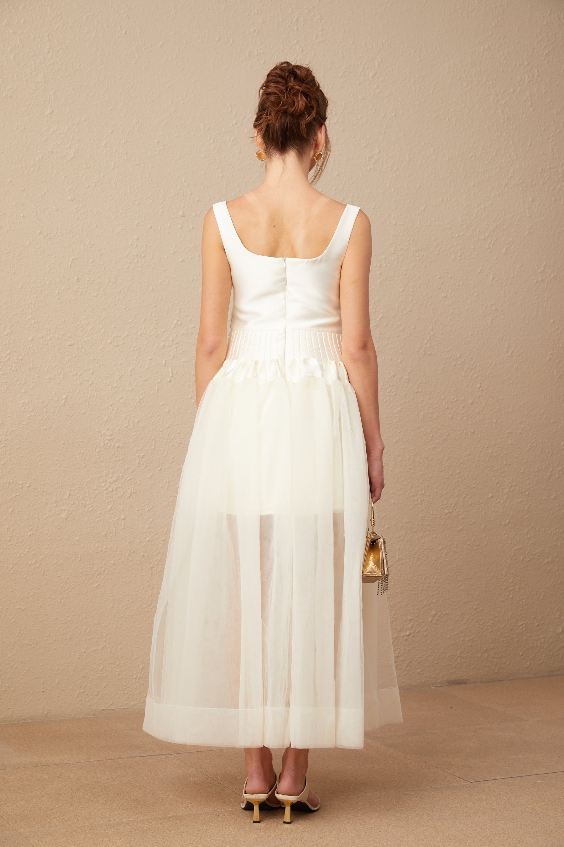 A woman wearing a long white satin and tulle maxi dress with panelled design standing in an elegant pose