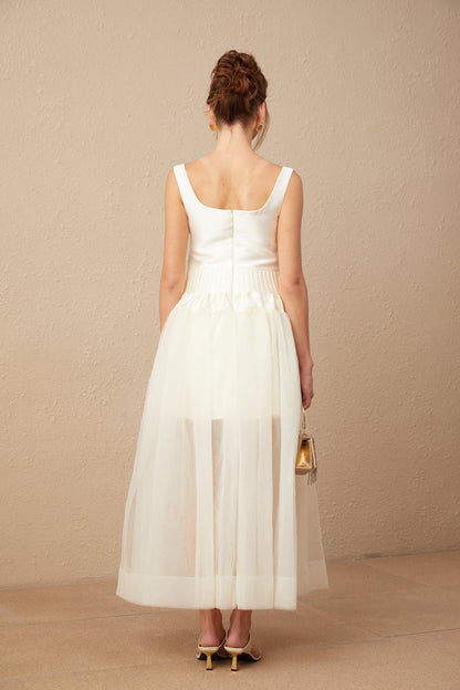 A woman wearing a long white satin and tulle maxi dress with panelled design standing in an elegant pose