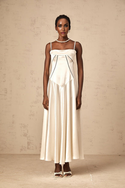 A woman wearing a long white satin dress with a flared skirt standing against a plain background